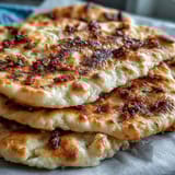 Buttery The Best Easy Garlic Naan Bread brushed with minced garlic, served warm beside a bowl of curry.