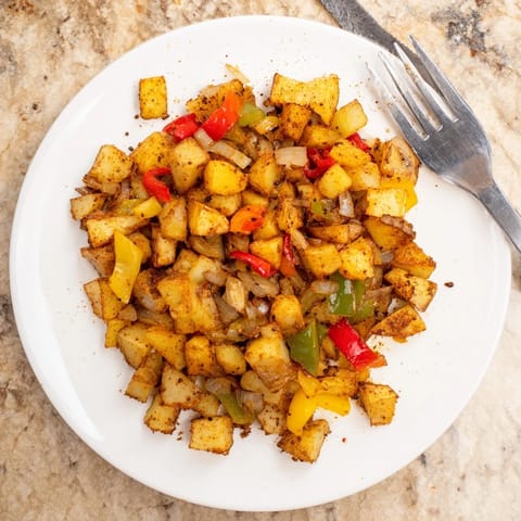 Golden-brown Home Fries sizzling in a cast iron skillet, mixing russet potatoes with diced red and green peppers. 