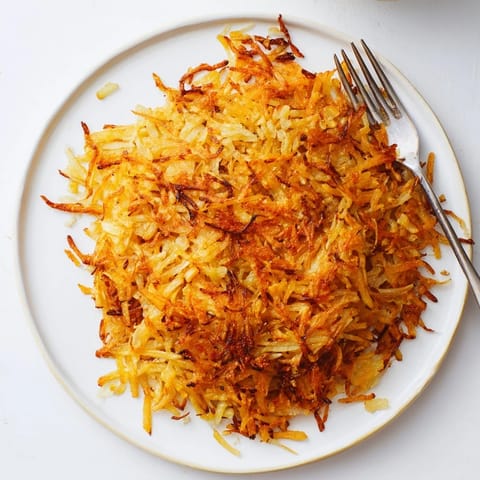 A plate of crispy Hash Browns served with sunny-side-up eggs, bacon, and fresh chives on a rustic table.