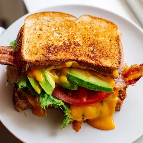 A close-up of a toasted Avocado BLT Grilled Cheese sandwich with creamy avocado, fresh lettuce, and sizzling bacon.