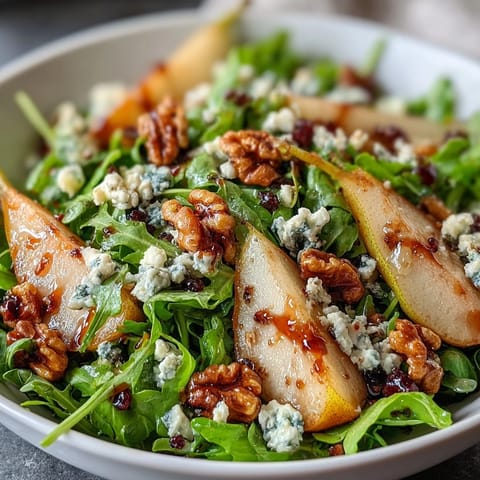 A vibrant arugula and pear bowl with creamy cheese and toasted nuts, drizzled with honey balsamic dressing.  