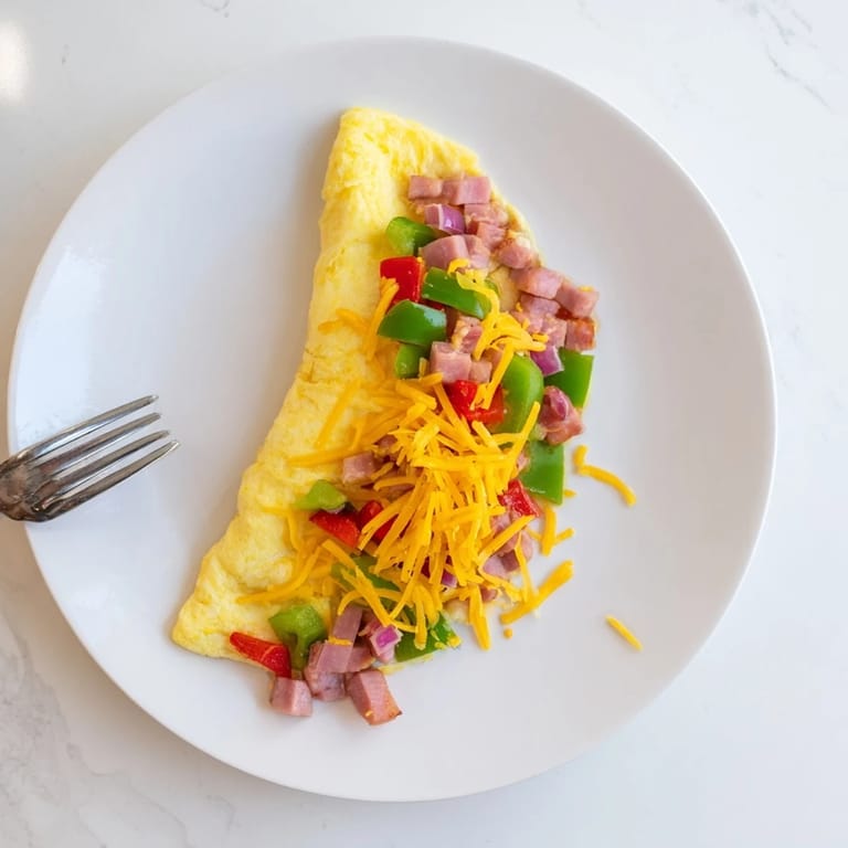 A fluffy Denver Omelet topped with sharp cheddar, served alongside crispy hash browns and fresh sliced tomatoes.