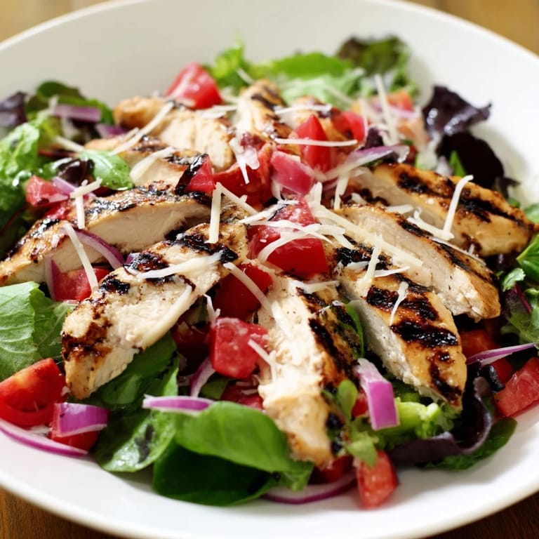 A close-up serving of Bruschetta Chicken Salad featuring tender herb-seasoned chicken, colorful bruschetta topping, and bright lemon wedges on a rustic plate.