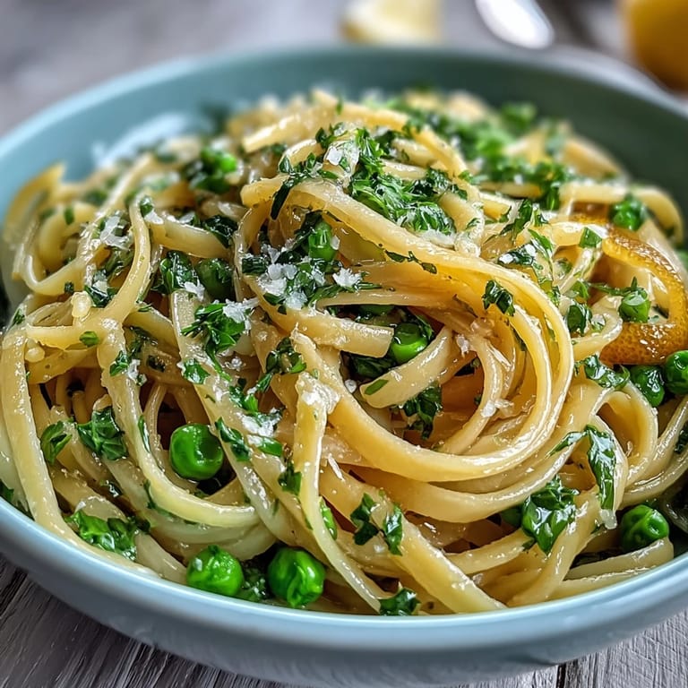 A bowl of lemon butter pasta with green peas, garnished with parsley and grated Parmesan cheese.