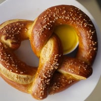 Golden-brown, twisted soft pretzels sprinkled with coarse salt, served warm alongside tangy yellow mustard.
