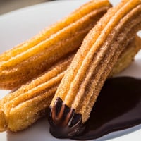 Golden-brown churros dusted in cinnamon sugar arranged next to a cup of rich chocolate dipping sauce.