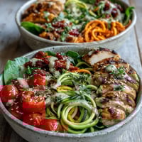A vibrant Spiralized Vegetable Bowl topped with grilled chicken, fresh cherry tomatoes, and a creamy tahini drizzle.