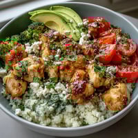 Steamed cauliflower rice bowl topped with grilled chicken, bell peppers, and fresh avocado slices.
